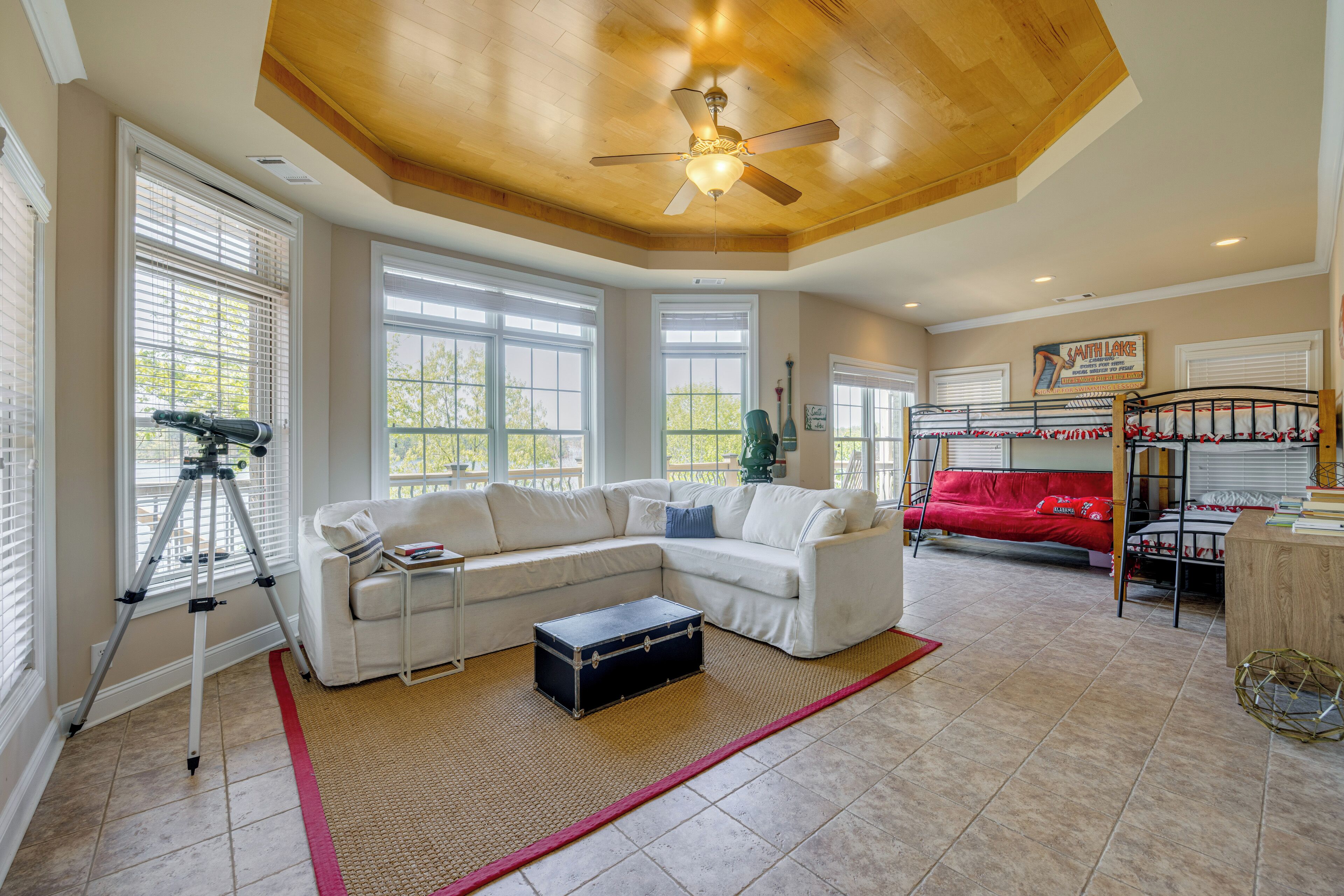 A spacious living room with a white sectional sofa, a red couch, a ceiling fan, and a telescope.