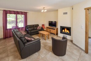 A living room with a sofa, a television, a fireplace, and a window with curtains. - Gite Aveyron  l'Orchis 8 pers Bezonnes Bozouls. 4 étoiles 4 épis. (Rodelle)