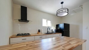 A modern kitchen with a wooden countertop, white cabinets, a black range hood, and a black refrigerator.