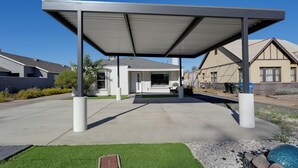 A covered outdoor area with a concrete floor, surrounded by a low white wall, and a small grassy area with a decorative stone feature.