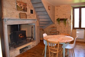 A rustic interior with a stone fireplace, a wooden table with chairs, a staircase, and a hanging plant. - Perigordian house in the countryside, calm and nature await you (Orliac)