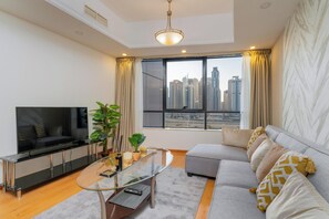 Ein modernes Wohnzimmer mit Flachbildfernseher, einem Glastisch, einem grauen Sofa und einem großen Fenster mit Blick auf die Stadt.