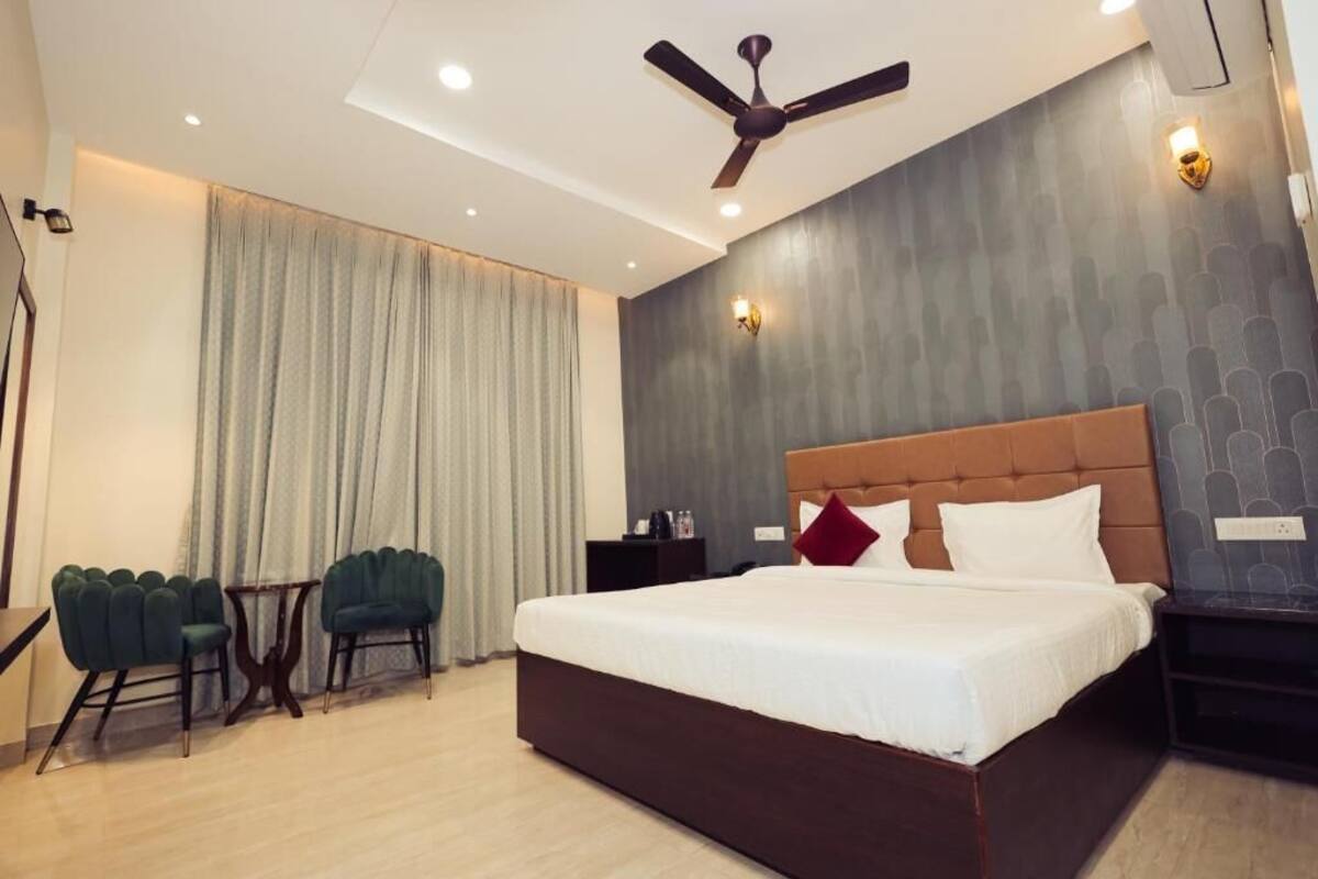 A hotel room with a large bed, two chairs, a ceiling fan, and a nightstand.