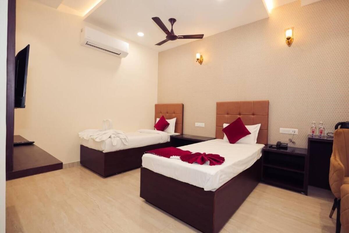 A hotel room with two beds, a ceiling fan, an air conditioning unit, a TV, and a small table with toiletries.