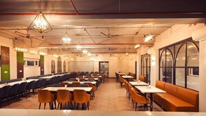 A restaurant with multiple tables and chairs, a long counter, and a large window. - HOTEL VANSHI VAT (Varanasi)