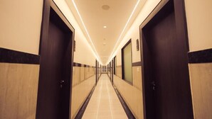 A hotel corridor with doors on both sides, a tiled floor, and a ceiling with recessed lighting. - HOTEL VANSHI VAT (Varanasi)