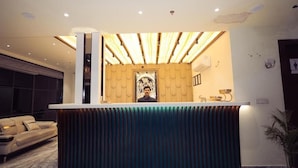 A reception desk with a modern design, a large framed picture above it, and a sofa in the background. - HOTEL VANSHI VAT (Varanasi)
