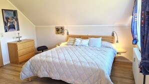 Een slaapkamer met een bed, een nachtkastje, een dressoir en een schilderij aan de muur.