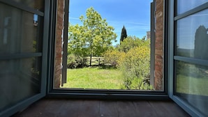 A window with a view of a grassy area, trees, and a distant building. - Casa Stella Serena by Geco Vacation Rentals (Chiusdino)