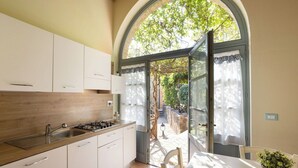 A kitchen with white cabinets, a gas stove, and a view through an open door to a garden. - Casa Stella Serena by Geco Vacation Rentals (Chiusdino)