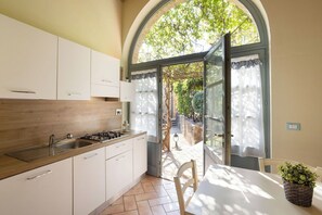 Eine Küche mit weißen Schränken, einem Gasherd und Blick durch eine offene Tür in einen Garten.