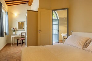 Ein Schlafzimmer mit einem Bett, einem Schreibtisch und einem Stuhl. Eine Tür führt in einen anderen Raum.