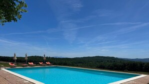 A rectangular swimming pool with clear blue water, surrounded by a tiled deck. There are lounge chairs and umbrellas along the poolside. - Casa Stella Serena by Geco Vacation Rentals (Chiusdino)