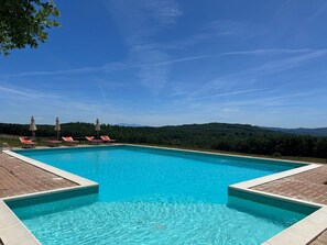 Ein rechteckiger Pool mit klarem, blauem Wasser, umgeben von einer gefliesten Liegefläche. Am Poolufer befinden sich Liegestühle und Sonnenschirme.