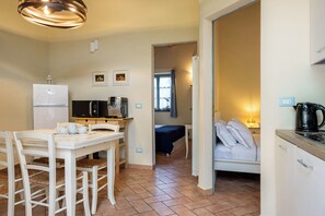 A compact kitchen with a refrigerator, microwave, and coffee machine. There is a dining area with a table and chairs, and a bed with pillows in the adjacent room. - Casa Stella Serena by Geco Vacation Rentals (Chiusdino)