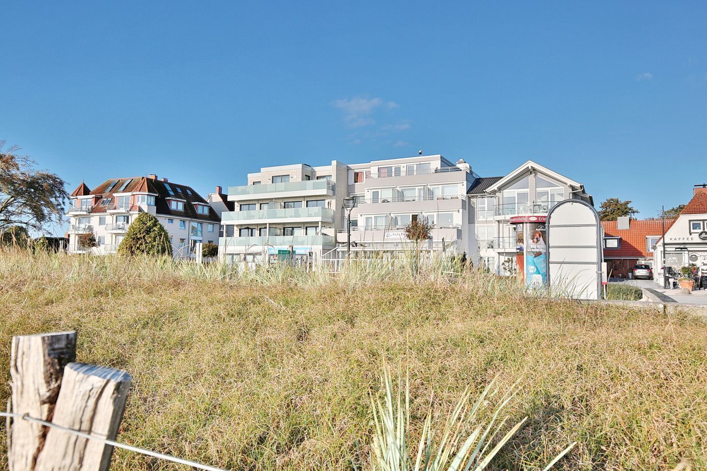A coastal residential area with modern buildings, a café, and a visible entrance gate.