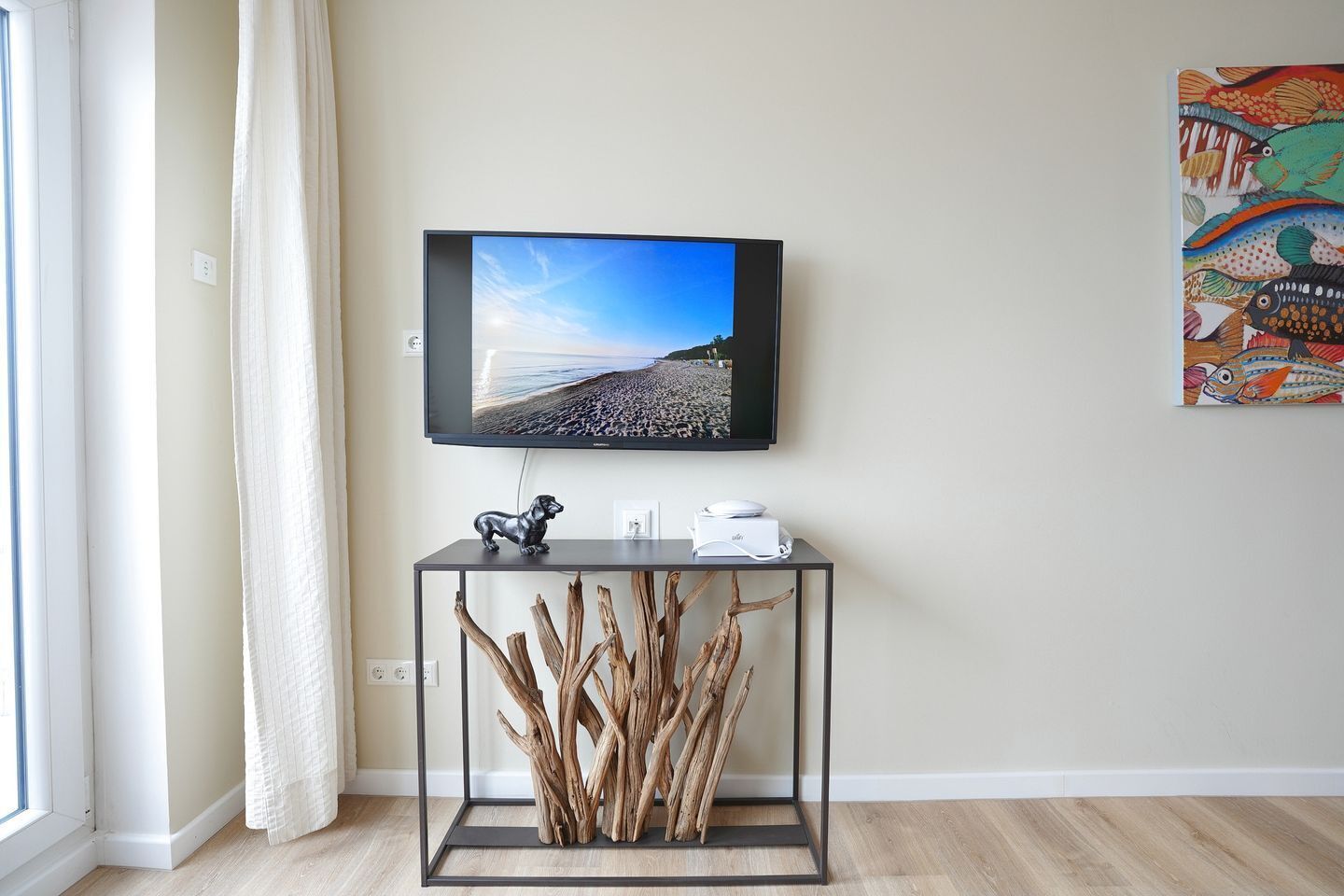 Une pièce avec un téléviseur accroché au mur, une console sur laquelle est posé un objet décoratif, et un tableau au mur.