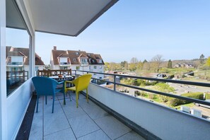 Un balcon avec une table et des chaises, donnant sur un quartier résidentiel avec des maisons et de la verdure.