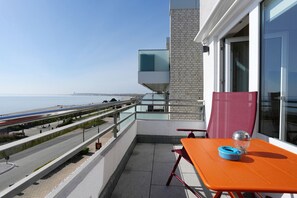 Un balcon avec une table et des chaises, une balustrade en verre et une vue sur la mer et un pont.