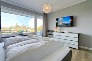 Ein modernes Hotelzimmer mit einem großen Bett, einem Flachbildfernseher, einem Schminktisch und Blick ins Freie.