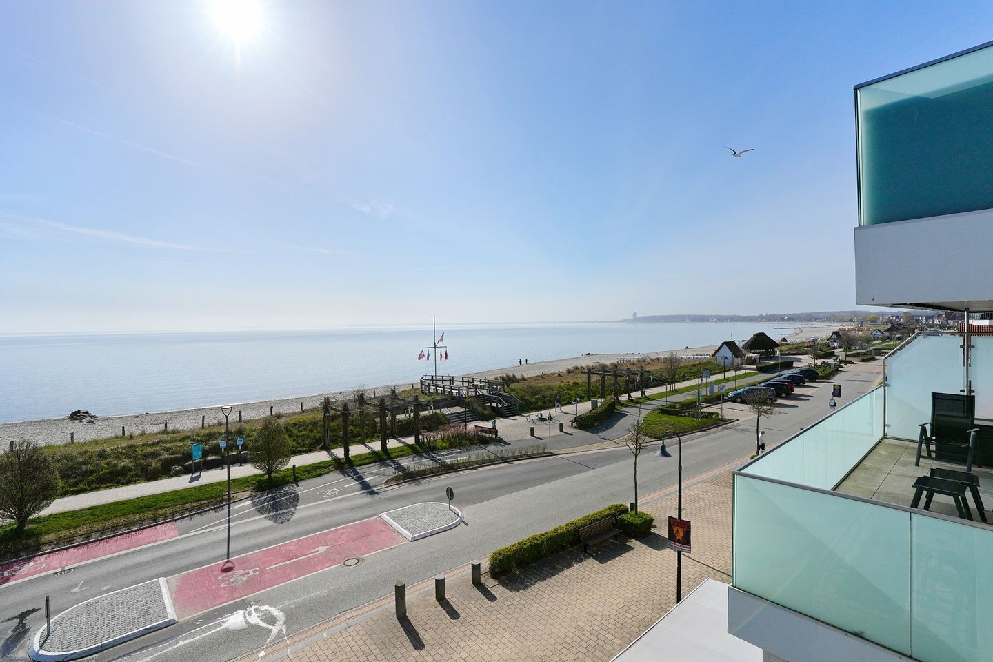A coastal view with a beach, a pedestrian path, and a modern building with a balcony.