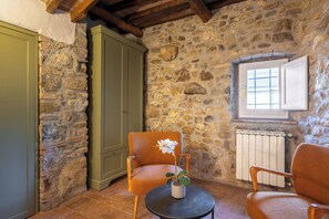 A rustic room with stone walls, a green cabinet, a wooden chair with a potted plant, and a window with blinds. - Maison Badia a Passignano, Alicante (Badia A Passignano)