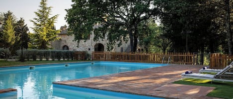 A swimming pool with a brick deck, surrounded by a wooden fence and trees.