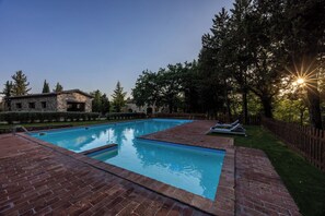 Una piscina rectangular con un borde de ladrillo, rodeada por una valla de madera y árboles.