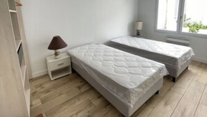 A bedroom with two beds, a nightstand, a lamp, and a window.