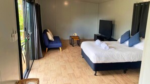 A bedroom with a bed, a TV, a small table, a chair, and a window with curtains. - Gunabul Homestead & Golf Course (Gympie)