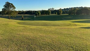A golf course with a clear sky, trees, and a well-maintained lawn. - Gunabul Homestead & Golf Course (Gympie)