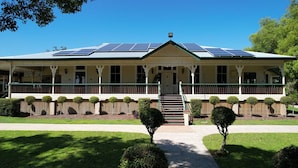 A two-story building with a covered porch, solar panels on the roof, and a well-maintained lawn with trimmed bushes. - Gunabul Homestead & Golf Course (Gympie)