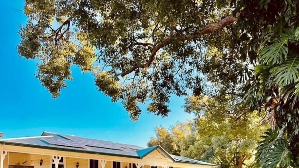 A two-story house with a covered porch, solar panels, and a well-maintained garden. - Gunabul Homestead & Golf Course (Gympie)