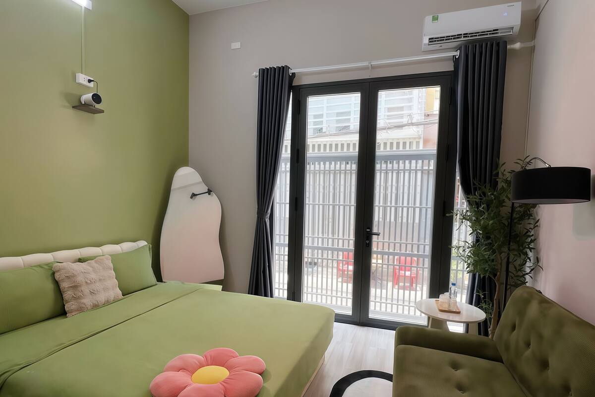 Ein Zimmer mit einem Bett, einem grünen Sofa, einem kleinen Tisch und Blick durch ein Fenster.