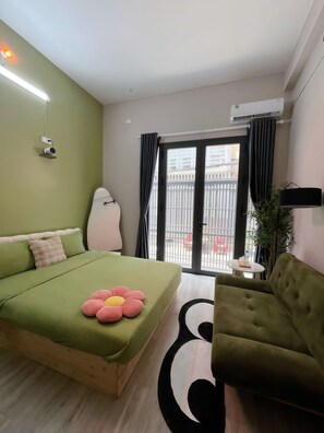 Quarto com cama, sofá verde, uma mesinha e vista pela janela.