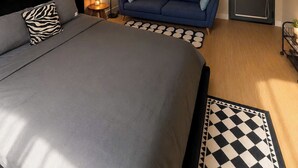 A hotel room with a bed, a sofa, a wall-mounted projector screen displaying 'NETFLIX', and a door with an air conditioning unit. - Trisstay Saigon - Dien Bien Phu (Ho Chi Minh City)