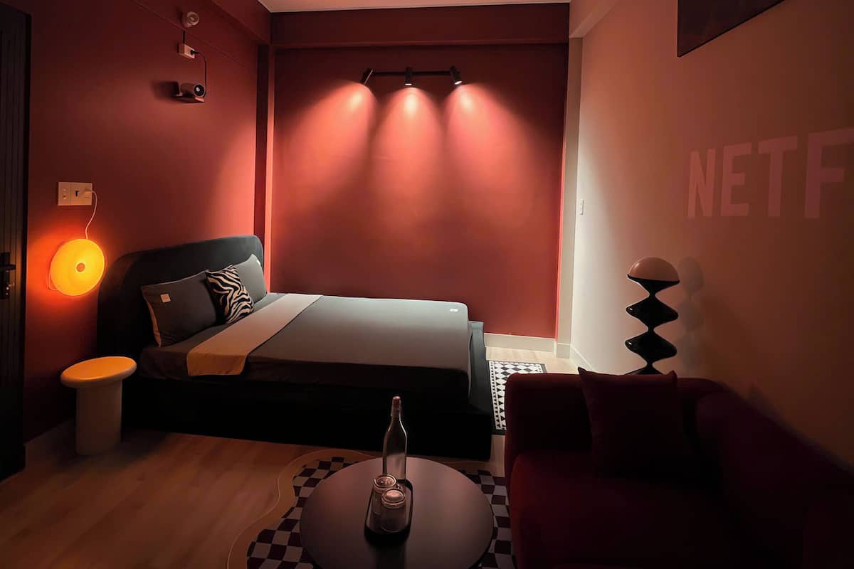 Ein modernes Hotelzimmer mit Bett, Couchtisch, Sofa, Fernseher und einem an der Wand montierten Projektor.