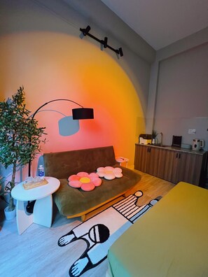 Quarto aconchegante com sofá, uma mesinha, uma planta e luminária na parede.