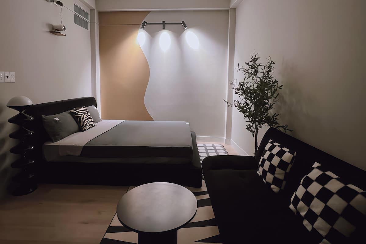 Ein modernes Zimmer mit einem Bett, einem Schlafsofa, einem kleinen Tisch und einer Pflanze.