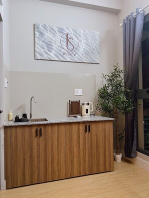 A modern kitchen with a marble backsplash, wooden cabinets, a kettle, and a potted plant. - Trisstay Saigon - Dien Bien Phu (Gia Dinh)