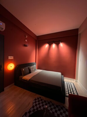 Quarto com uma cama, luminária na parede e tapete xadrez.