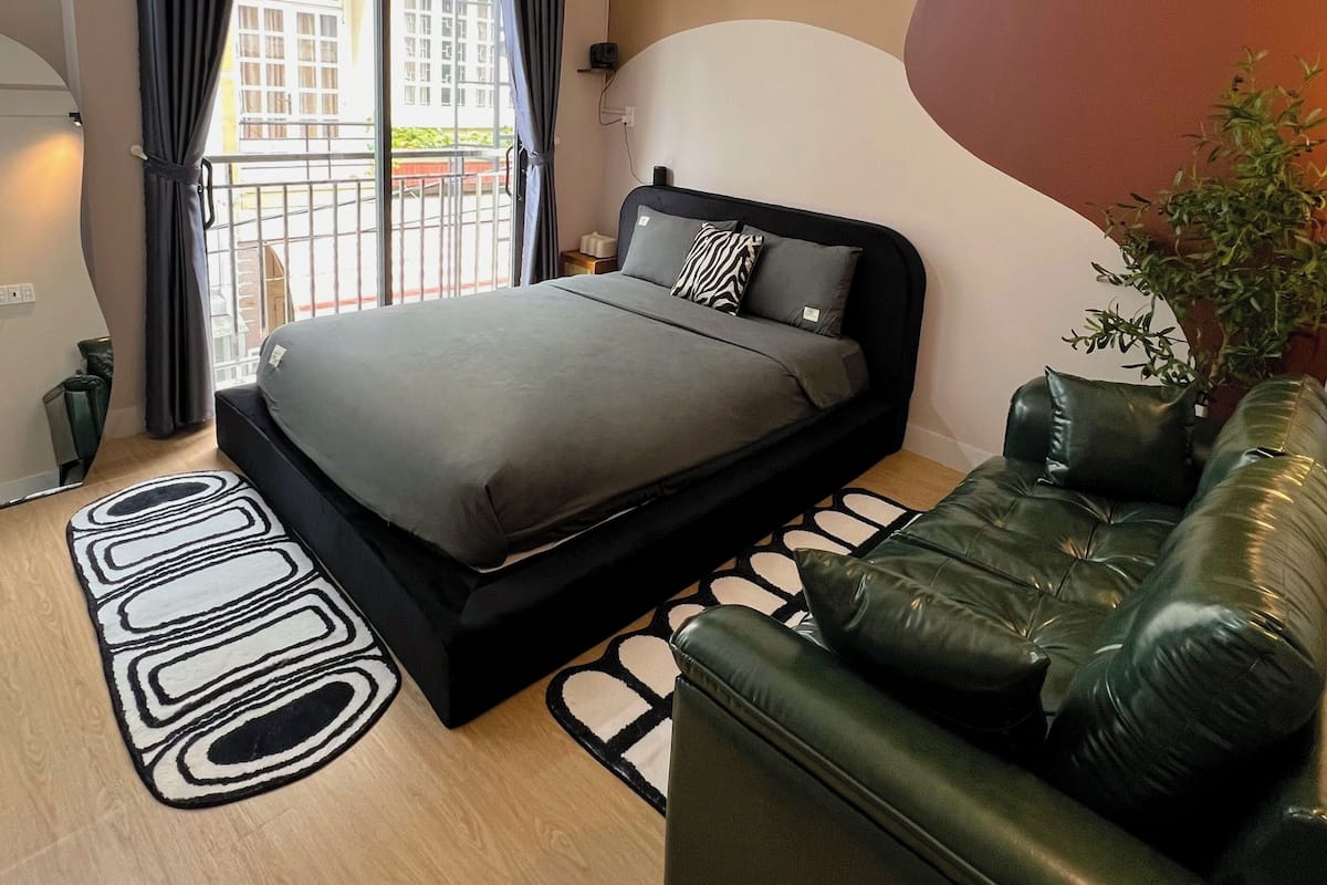 Ein modernes Schlafzimmer mit Bett, einem grünen Ledersofa, einem großen Fenster mit Vorhängen und einem Balkon.