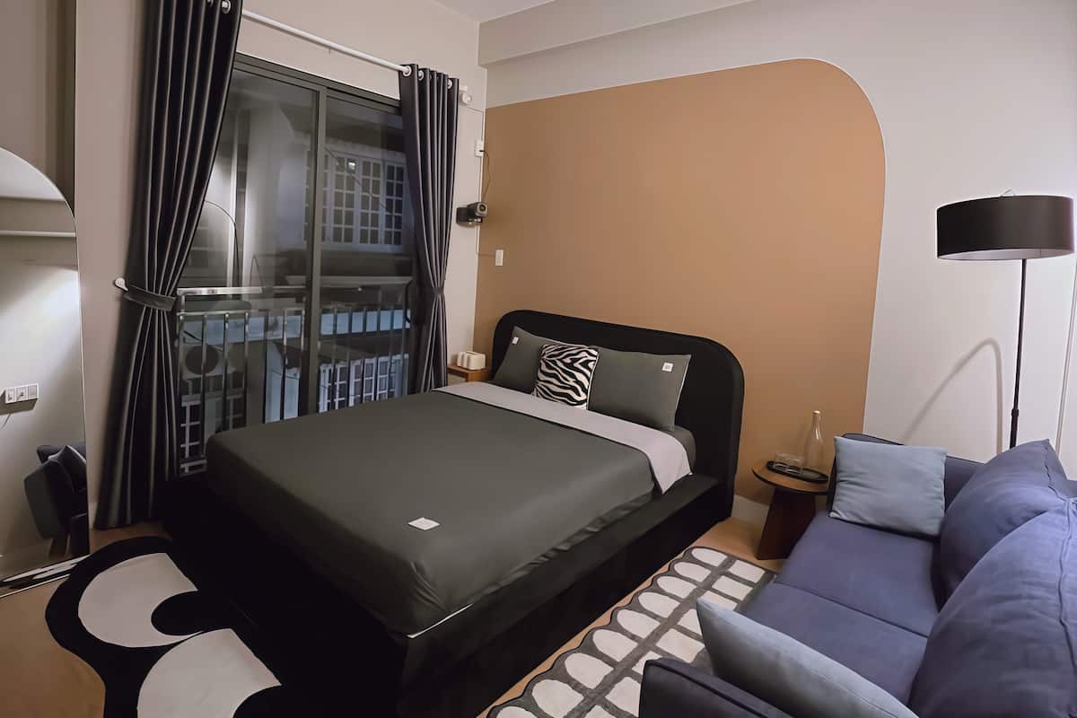 Ein modernes Hotelzimmer mit Bett, Sofa, Lampe und Blick ins Freie.