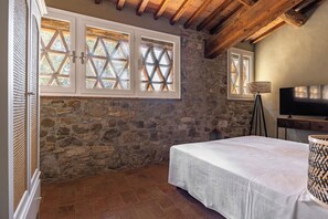 Ein Schlafzimmer mit Steinwänden, einem Bett, einem Fernseher und einem Fenster mit Holzgitter.