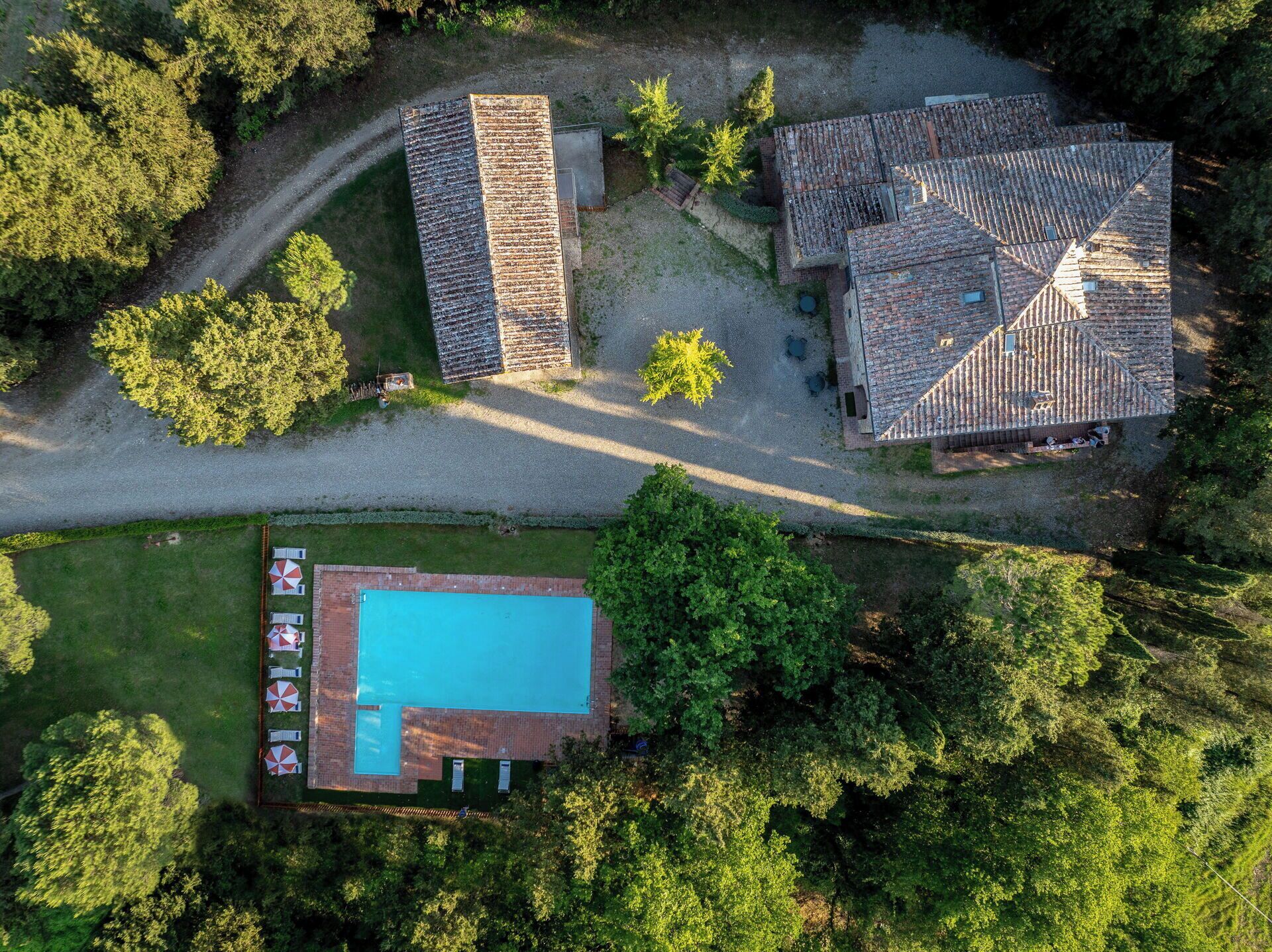 An aerial view of a property with a swimming pool, a large building with a tiled roof, and surrounding greenery.