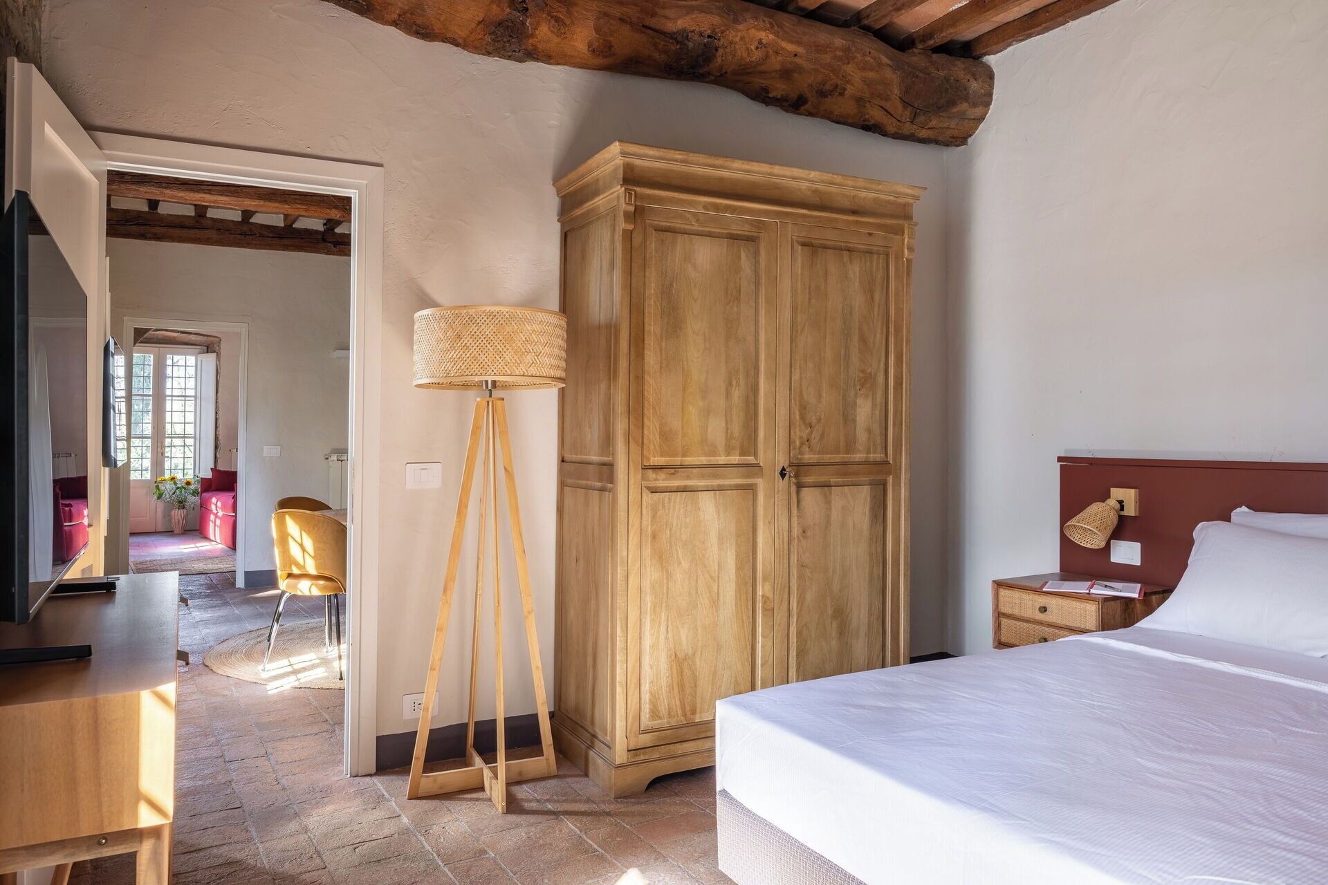 A bedroom with a bed, wooden wardrobe, floor lamp, and a desk with a lamp.