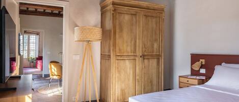 A bedroom with a bed, wooden wardrobe, floor lamp, and a desk with a lamp.