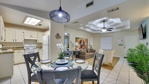 A modern kitchen with white cabinets, a dining table with chairs, a ceiling fan, and a living area with a couch and a painting. - Pool Access & Work-Ready Comforts! Edinburg Apt (Edinburg)