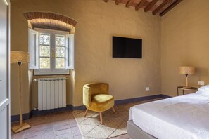 A bedroom with a bed, a chair, a radiator, a window, and a wall-mounted TV. - Apartment in Badia A Passignano with 3 bedrooms sleeps 6 (Badia A Passignano)