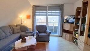 A living room with a sofa, armchair, coffee table, and a TV. - Appartmenthaus Nolting Apartment 3 Nolting: 40 m² with terrace and WLAN - (Werdum)
